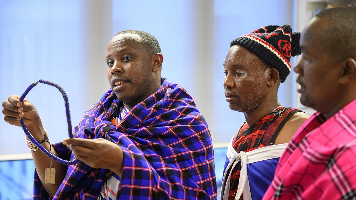A Maasai man talking while presenting an object