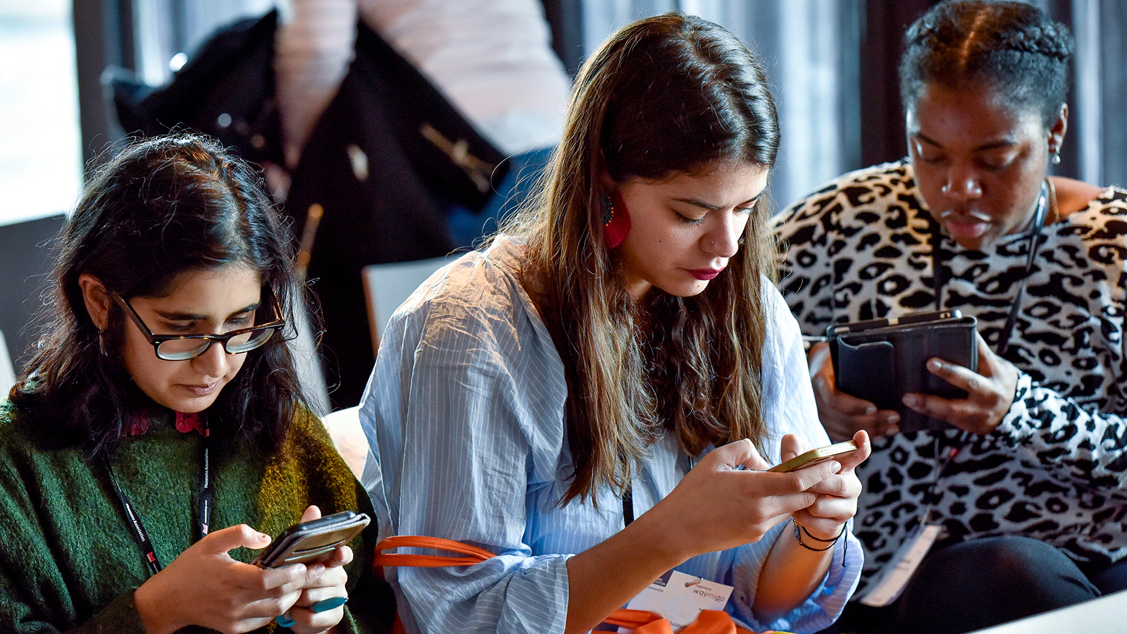 Three people look at their smartphones while sitting in a row