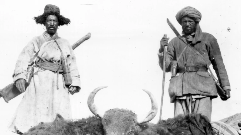 Two men stand over a dead yak