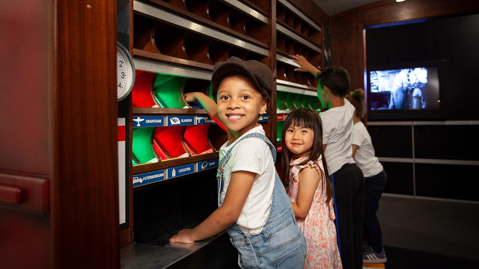 Two children smile while engaging with a museum exhibition at the Postal Museum