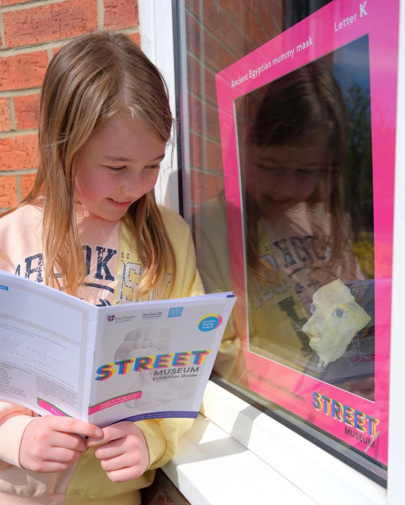 A child with long hair looks at an exhibition in a window