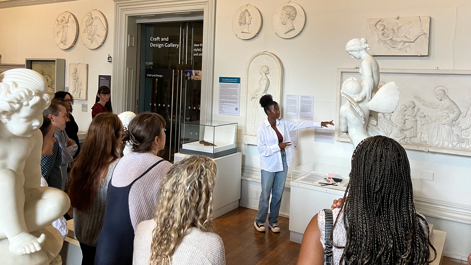 A person leads interpretation of a large white sculpture, talking to a crowd of people