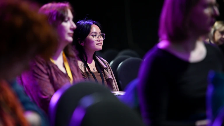 A person sits and smiles while in a darkened auditorium space at Conference 2024