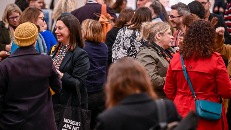 A crowd of people, dressed in winter clothing, engage in conversation at an MA conference