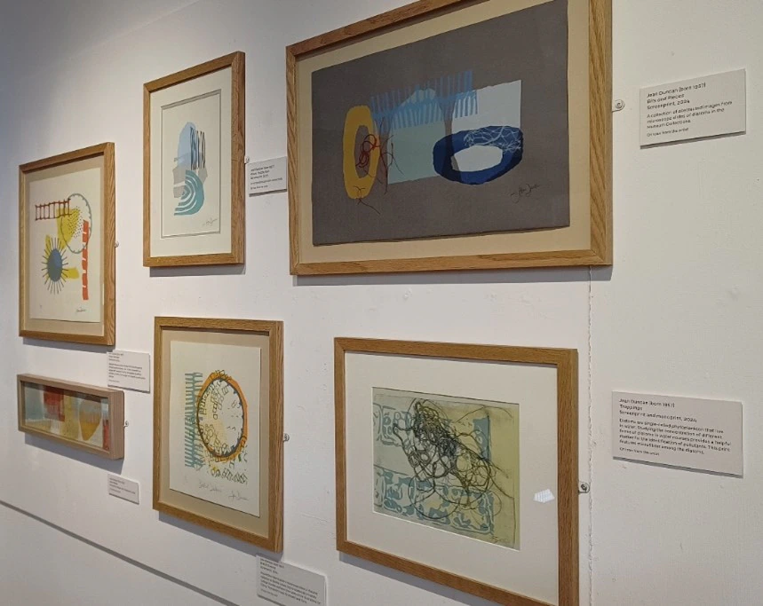 Framed abstract artworks are displayed in two rows on a white gallery wall