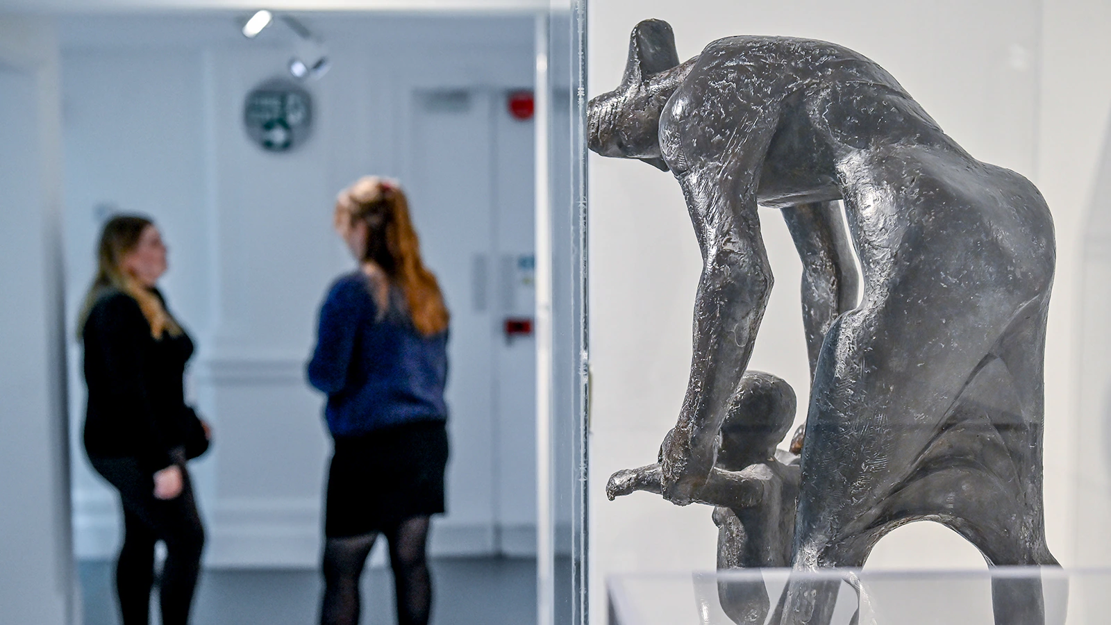 Two people stand and talk near a glass display case with a sculpture