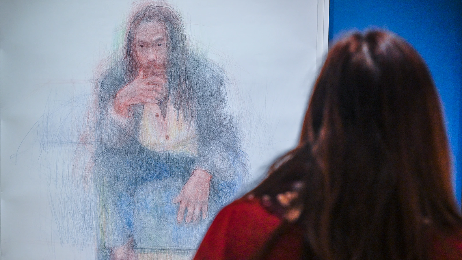 A person looks at a pencil drawing of a man in a suit sitting, his hand at his mouth