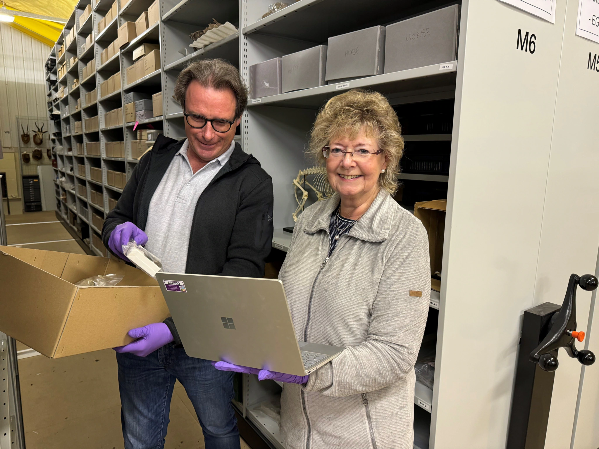 A man and a woman smile in a museum storeroom