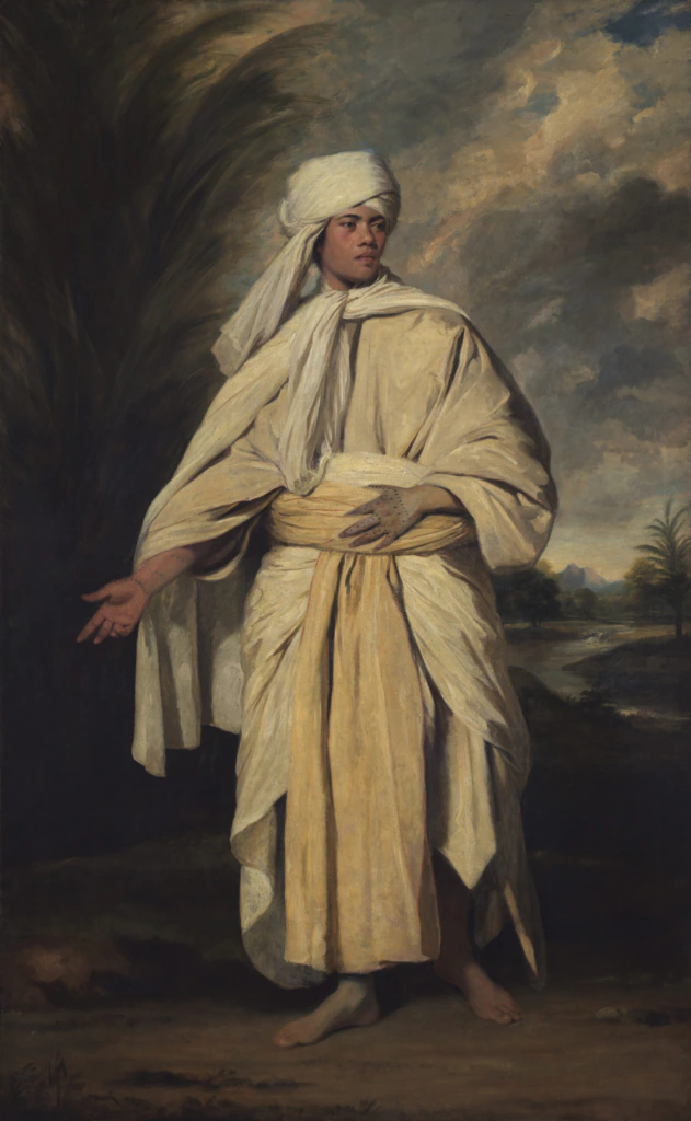 A person stands outdoors wearing traditional North African or Middle Eastern robes and a white turban, with bare feet. The background features dark clouds, palm trees, and a distant landscape.