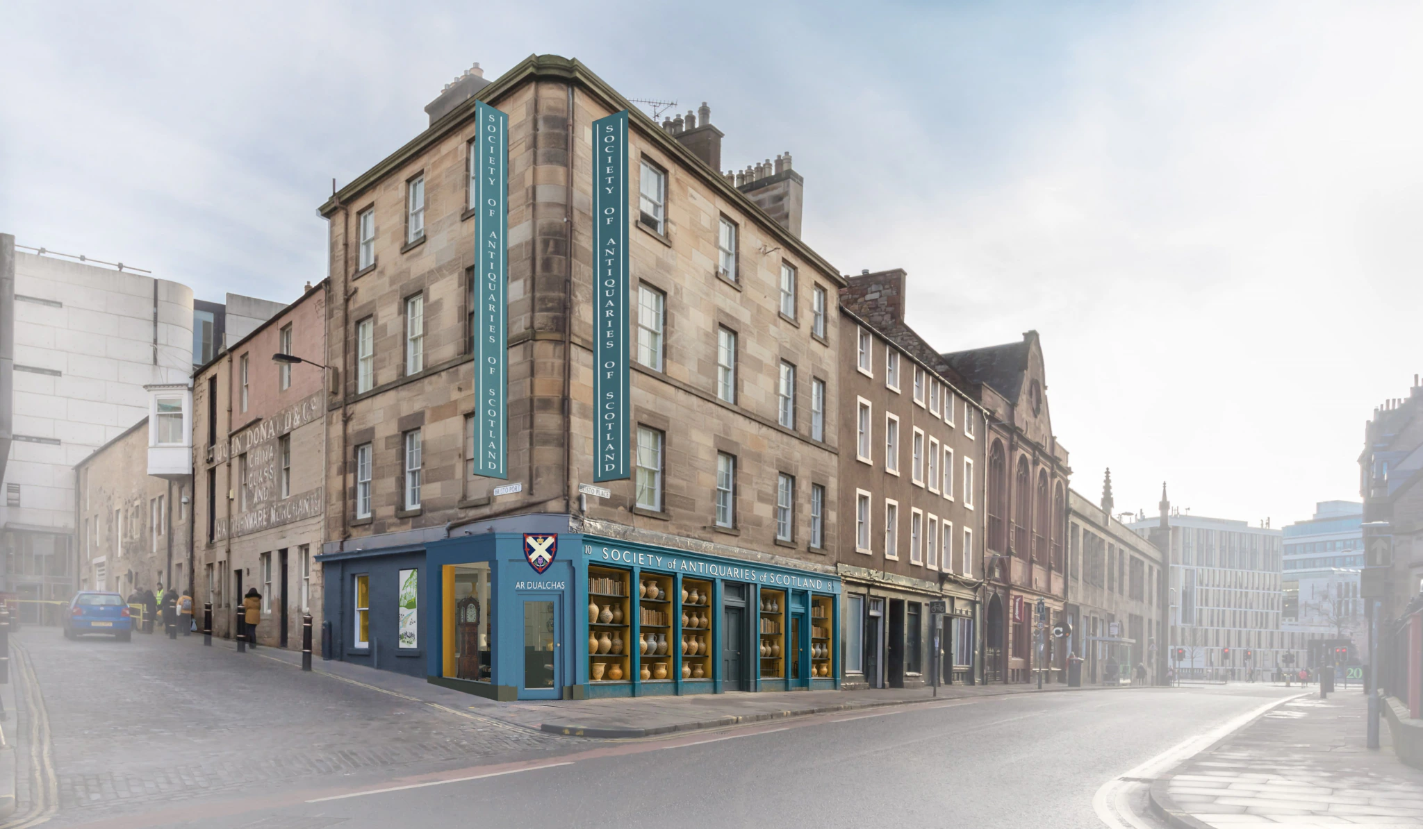 A street corner with a historic stone building featuring large windows and blue signs reading Society of Antiquaries of Scotland. The street is mostly empty, and the sky is slightly overcast.