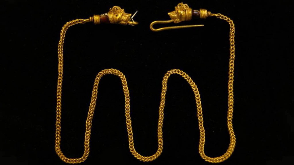 A gold chain with intricate links, ending in ornate animal or mythical creature heads, with a hook clasp on one end, displayed against a black background.