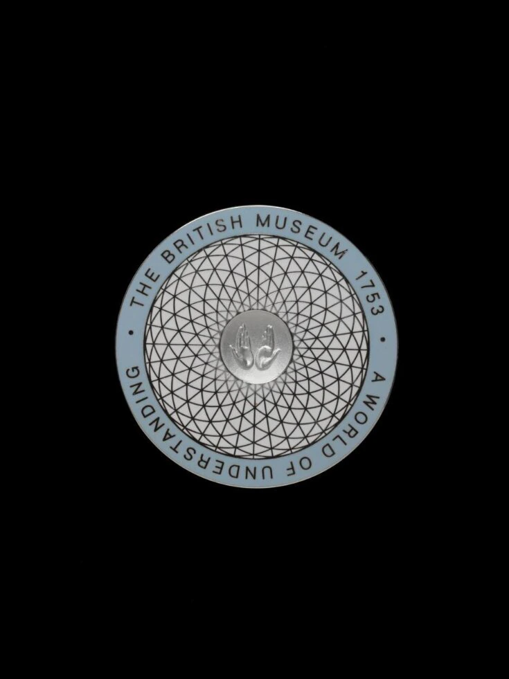 A circular badge with a geometric pattern, the British Museum logo in the center, and the text THE BRITISH MUSEUM 1753 A WORLD OF UNDERSTANDING around the edge on a black background.
