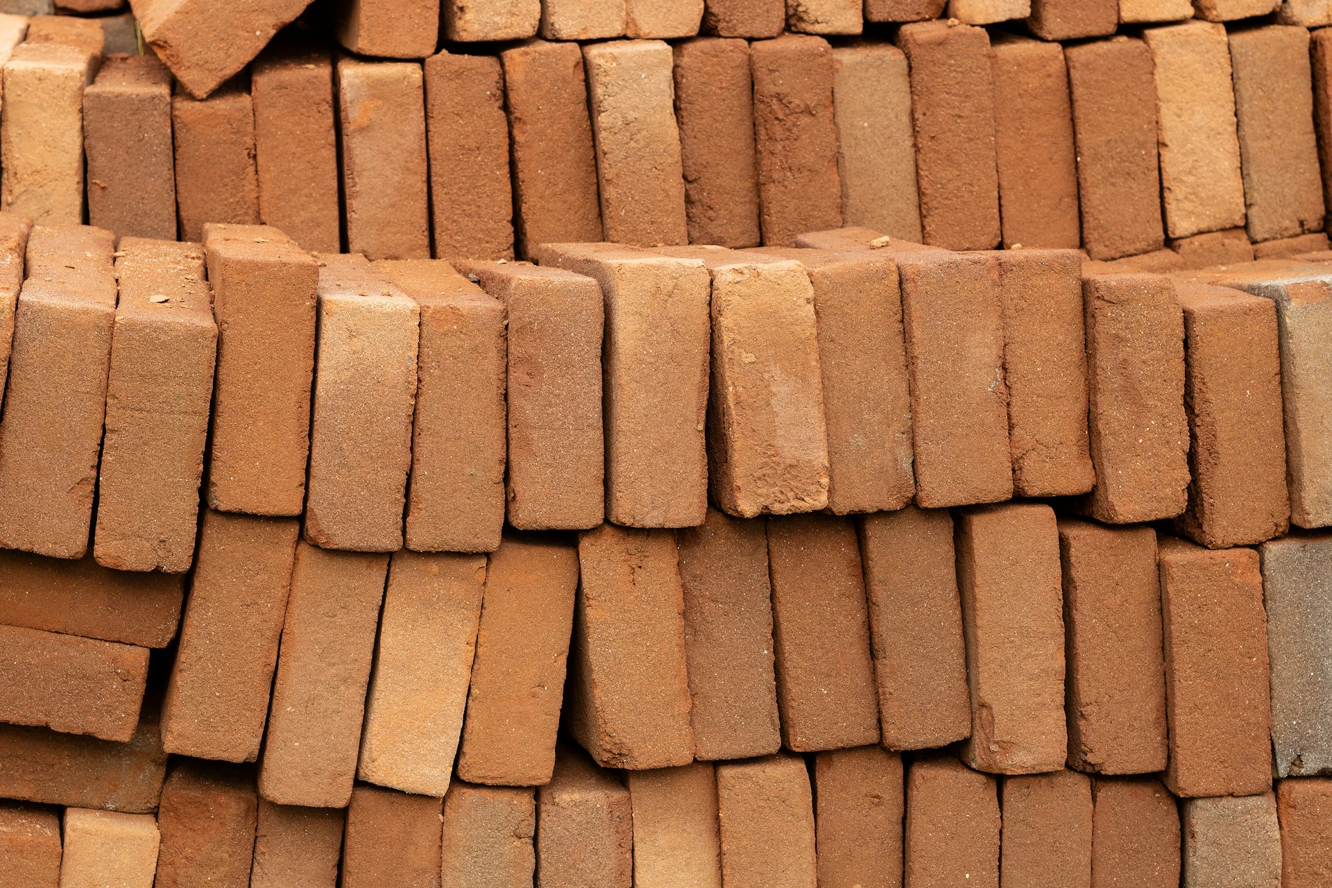 A close-up view of multiple stacks of reddish-brown rectangular bricks arranged in an orderly, horizontal pattern.