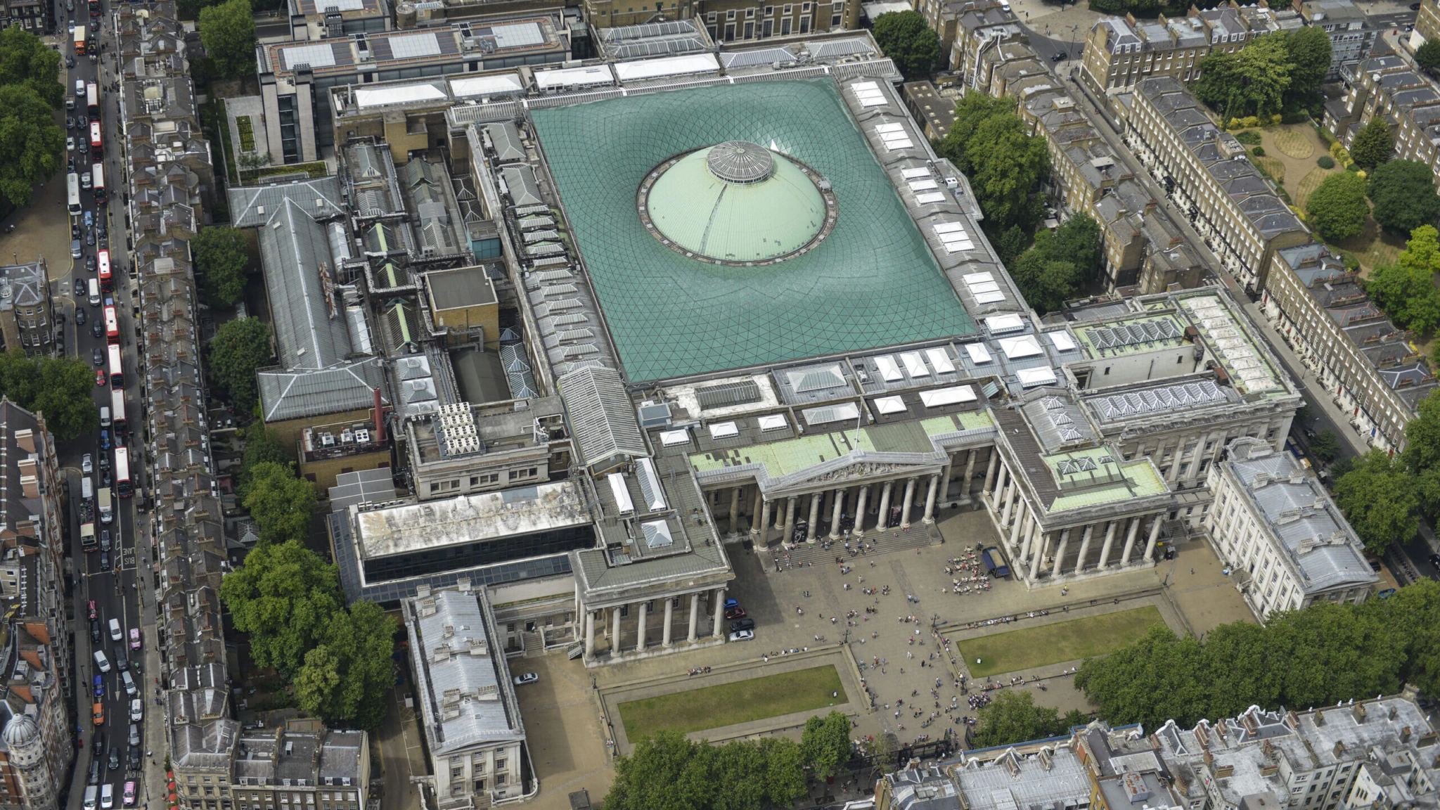 Aerial view of the British Museum in London, featuring its large central glass-roofed courtyard surrounded by classical buildings and tree-lined streets.