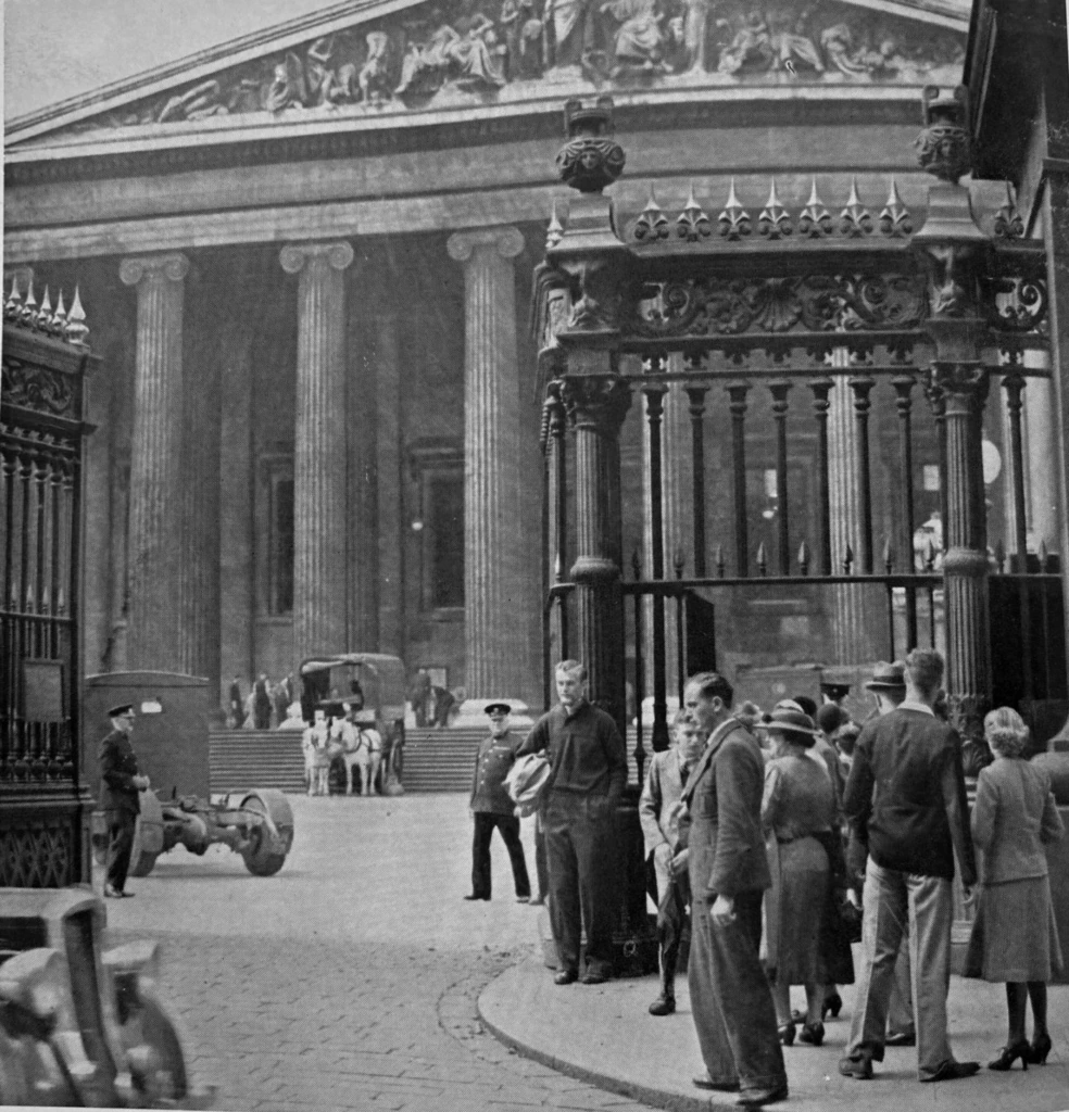 Black and white photo of people gathered outside the British Museum’s entrance, with large columns visible. Caption below reads: “THE BRITISH MUSEUM AND THE WAR Removing material from the Museum at the end of August.”.