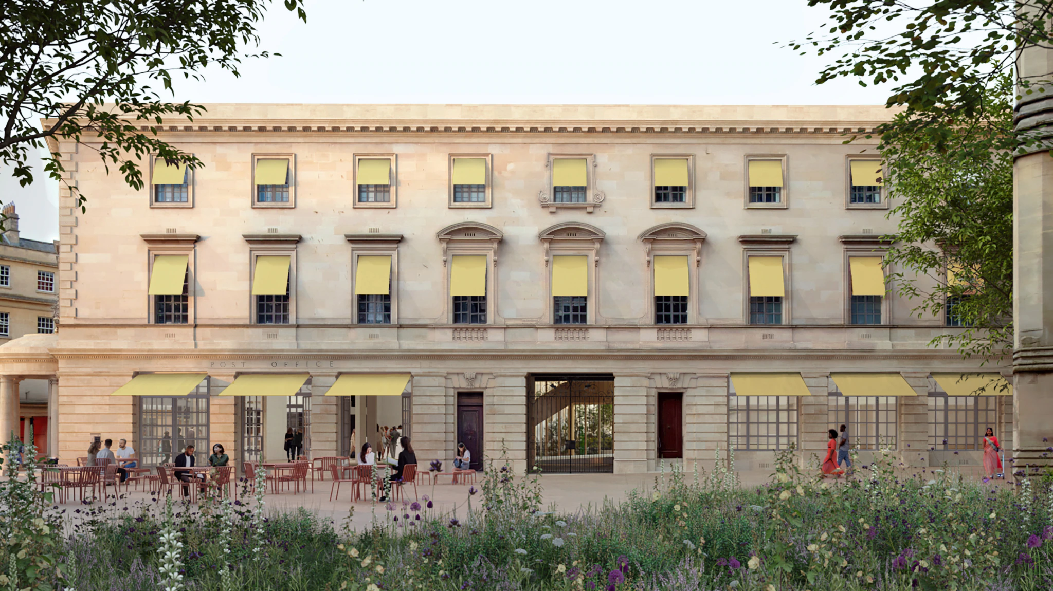 A three-story classical building with yellow window awnings; people sit at outdoor tables and walk nearby, surrounded by greenery and wildflowers in the foreground.