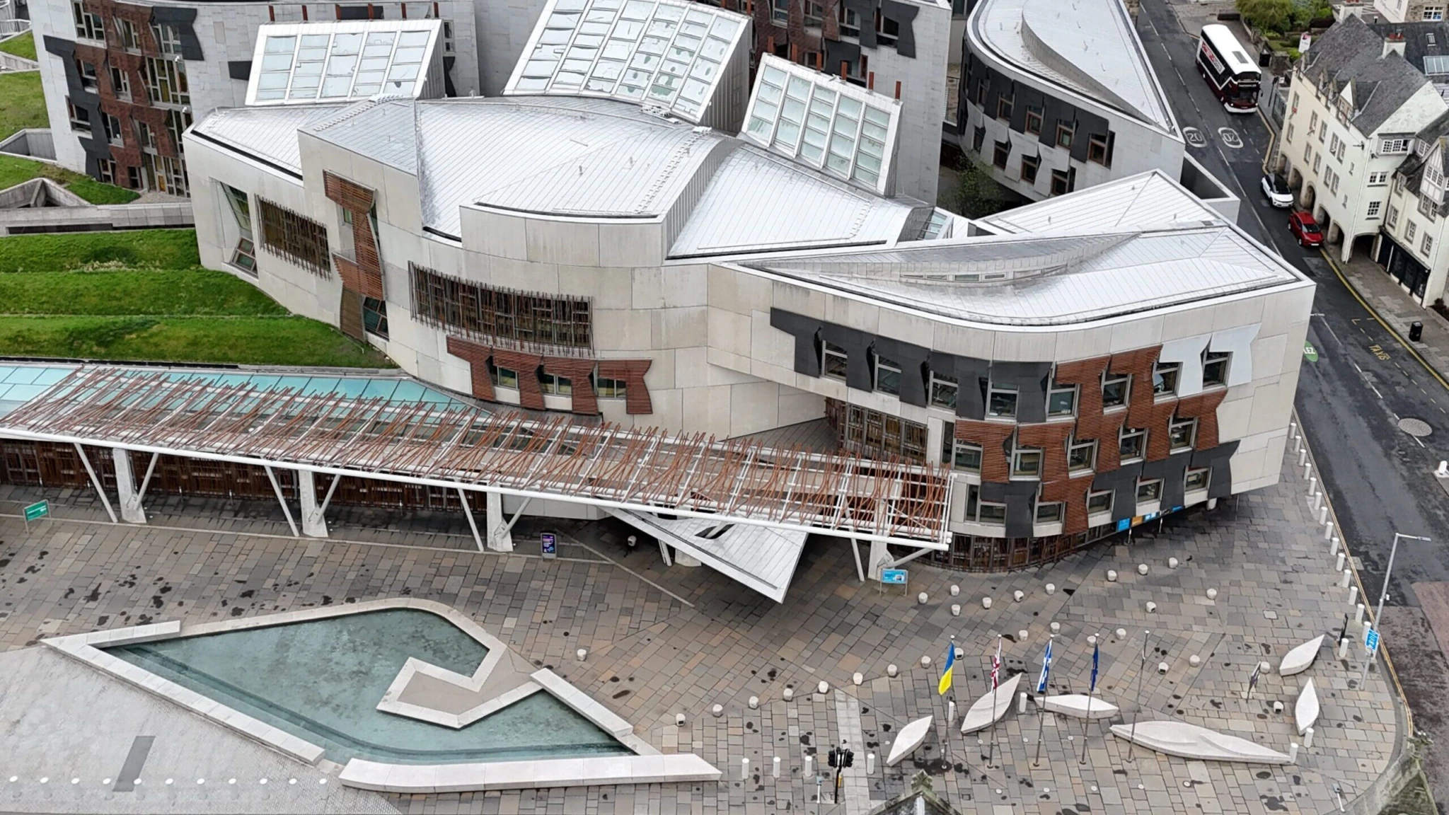 Aerial view of the Scottish Parliament building in Edinburgh, featuring modern, angular architecture with white roofs, a courtyard, and surrounding city streets and residential buildings.