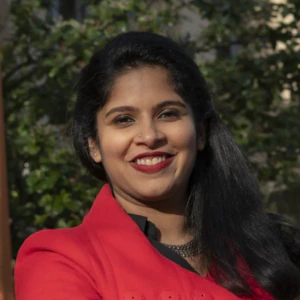 A woman wearing a bright red coat smiles while standing outside.