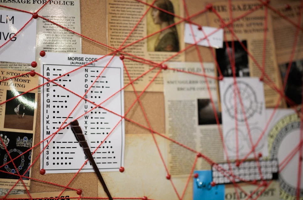 A corkboard with newspaper clippings, a Morse code chart, photos, and documents connected by red string, resembling a crime investigation board.