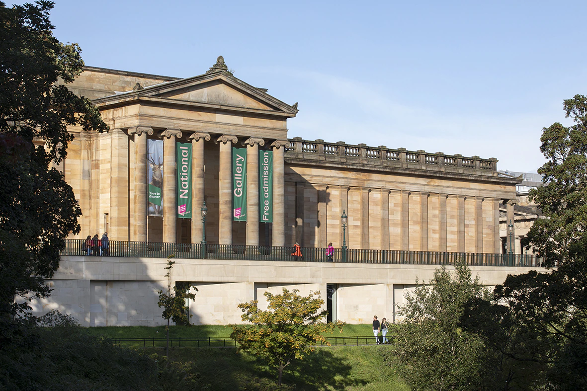 A neoclassical building with large columns displays banners reading National Gallery and Free Admission. People walk along the terrace. Green trees and grass surround the structure.