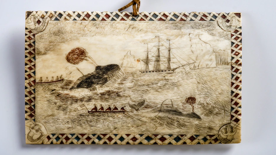 Rectangular scrimshaw plaque showing a whale hunt: sailors in rowboats chase whales, one spouts blood. A sailing ship and cliffs are in the background. The border has a geometric pattern and a small rope loop at the top.