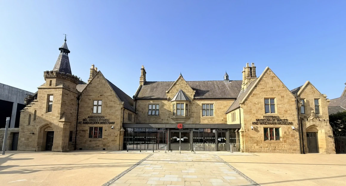 A historic stone building with peaked roofs, a small turret, and signs reading Middlesbrough Museums on the facade, set against a clear blue sky.