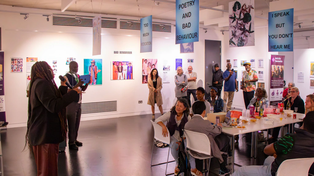 Someone speaks to a group of people sat at a table in a gallery space