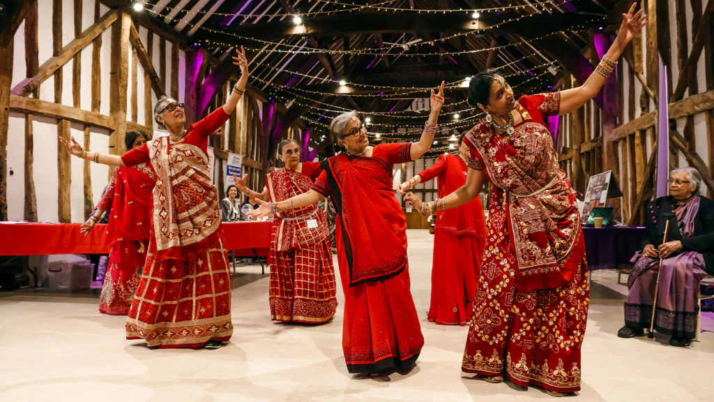 Dancers in brightly-coloured dresses perform in a timber-framed museum space