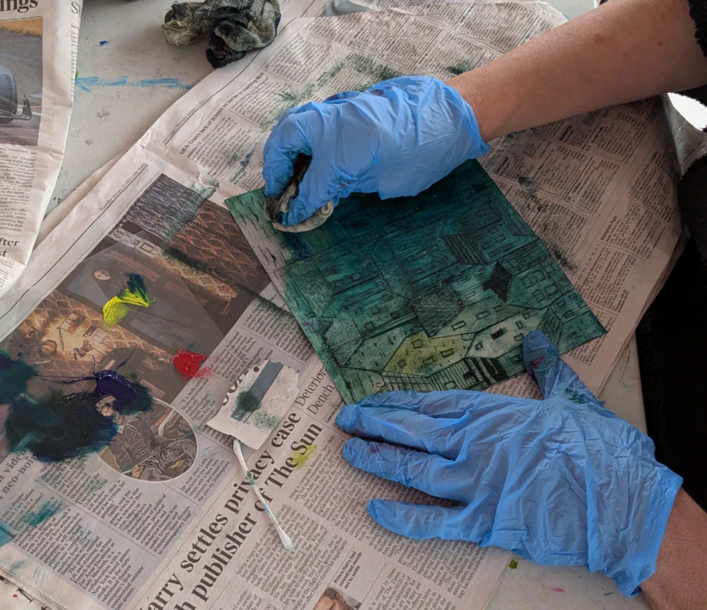 A person wearing gloves and working on a small painting with blues and greens