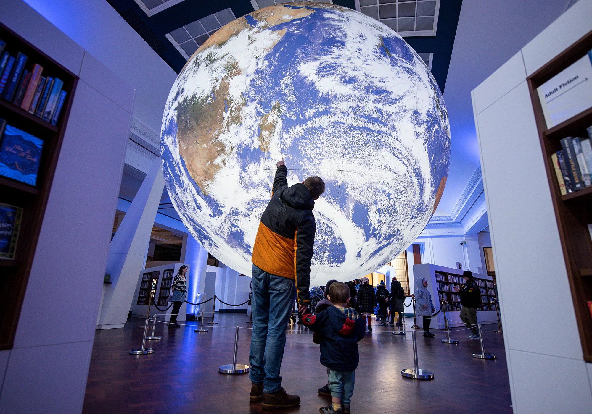 A man and small child stand in front of a big model of the Earth
